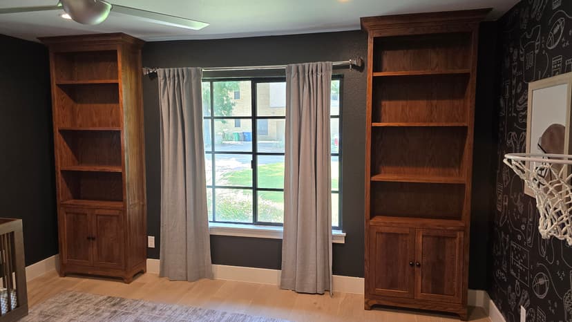 Pair of stained oak built-in bookcases with crown flanking a window