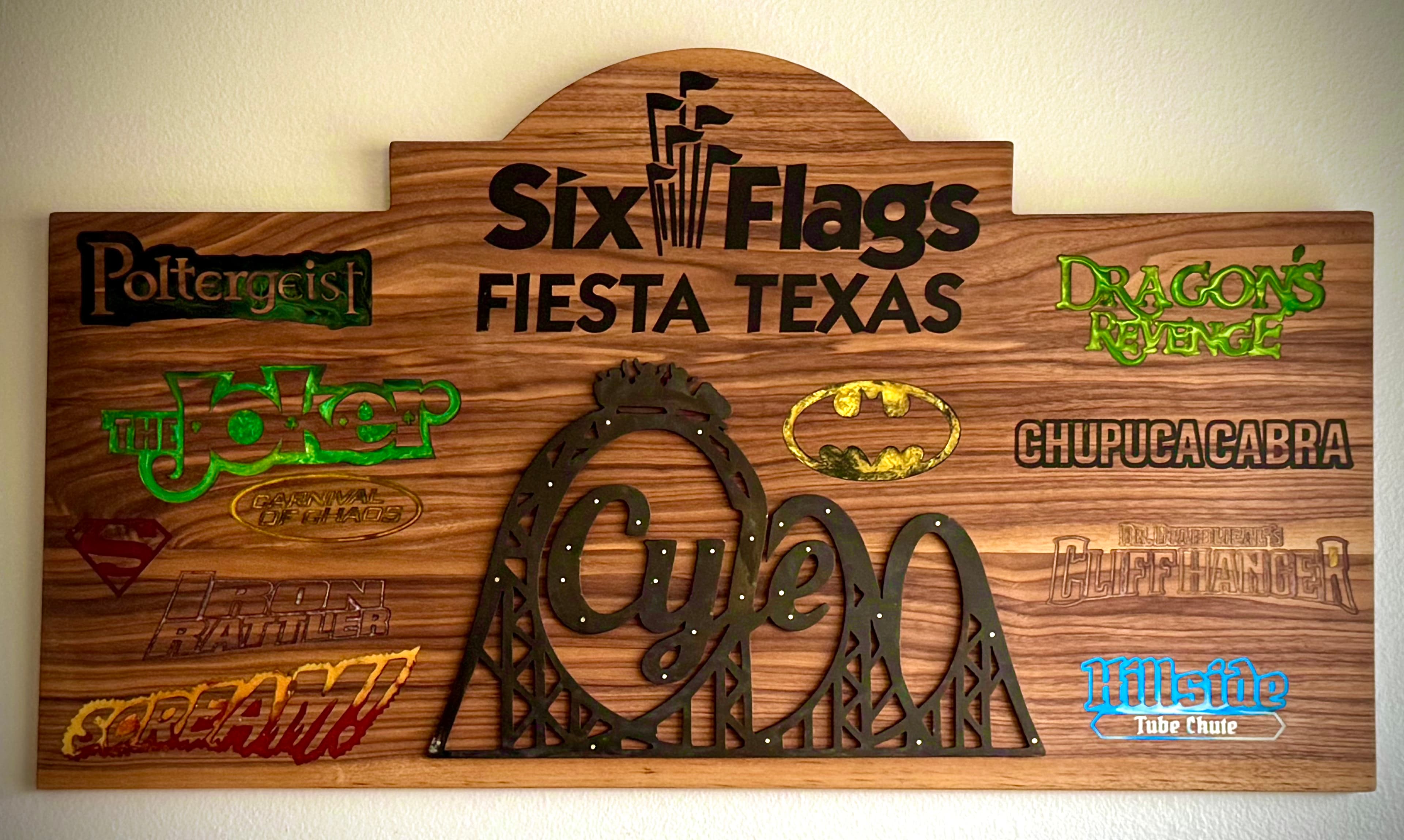 Custom CNC engraved walnut sign featuring Six Flags Fiesta Texas ride logos with colored epoxy fills. A collaboration with Black Dog Forge, who handled the epoxy work and plasma cut the central roller coaster emblem. Each ride logo was precision-engraved and filled with matching epoxy colors.