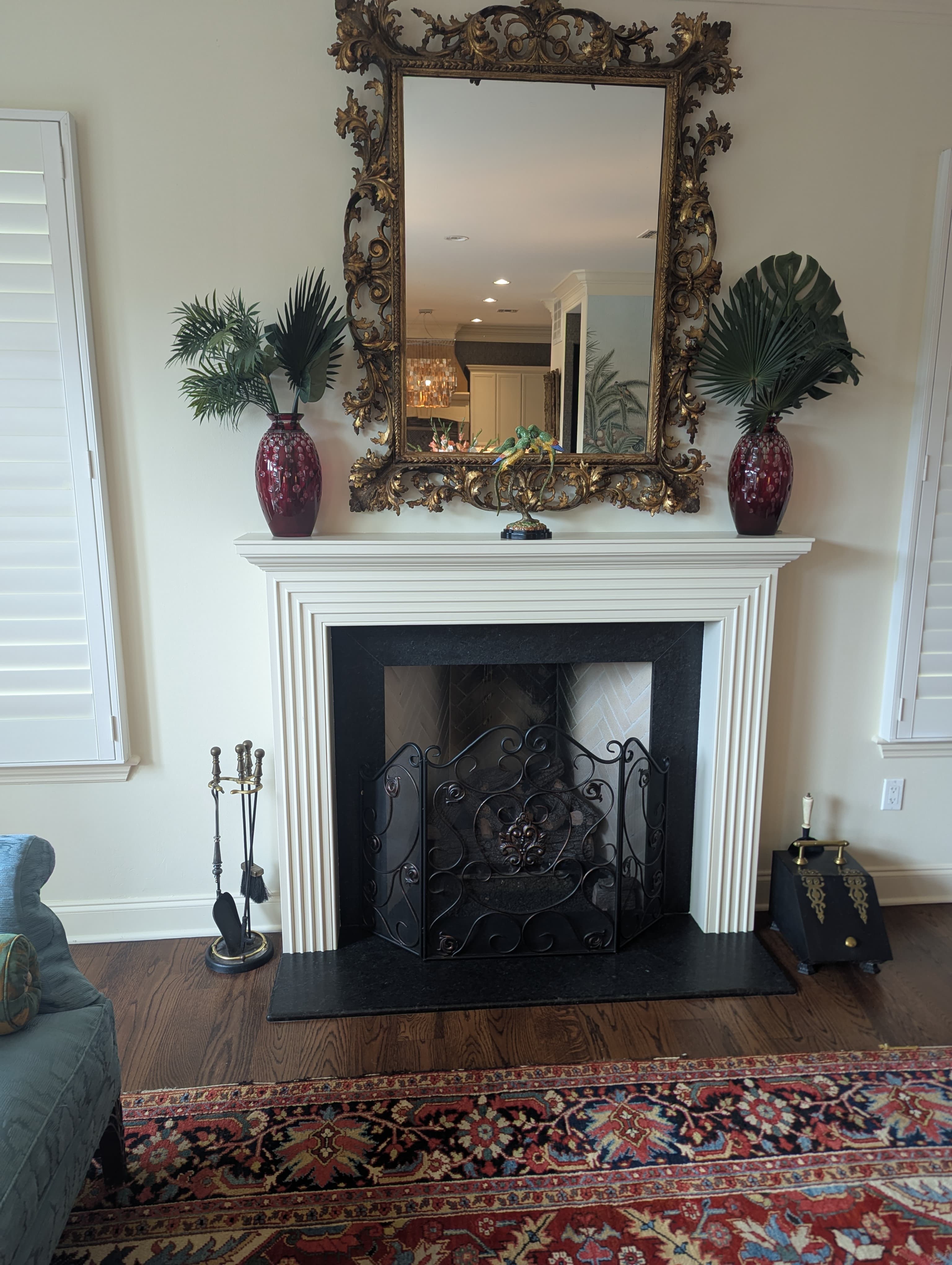 Stunning custom fireplace mantel featuring intricate white fluted trim work and classical millwork details. The timeless design includes a custom-built mantel shelf perfect for display, black marble surround, and decorative wrought iron screen. This elegant focal point showcases expert carpentry craftsmanship and attention to detail.