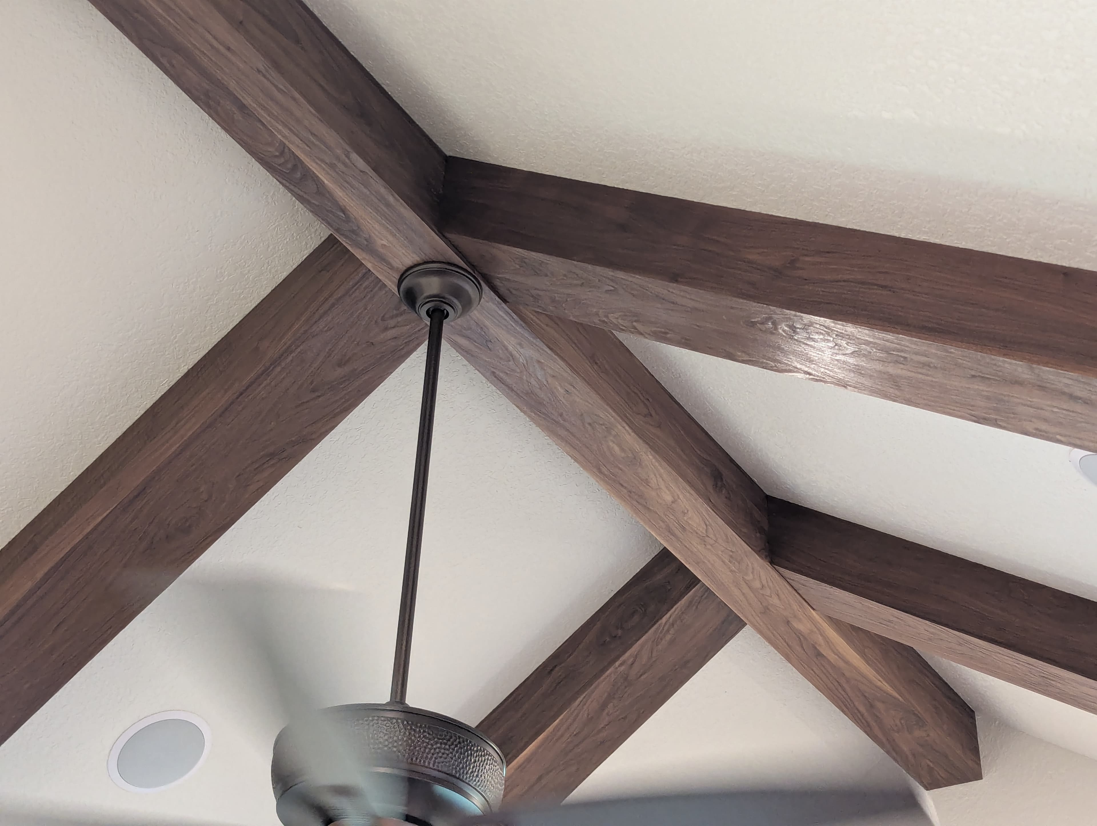 Close-up detail of custom distressed walnut beam wraps showing the natural grain pattern and lacquer finish. The intersecting beam joints are precision-fitted, and the distressing technique brings out the character of the walnut while the lacquer provides a subtle sheen and protects against wear.