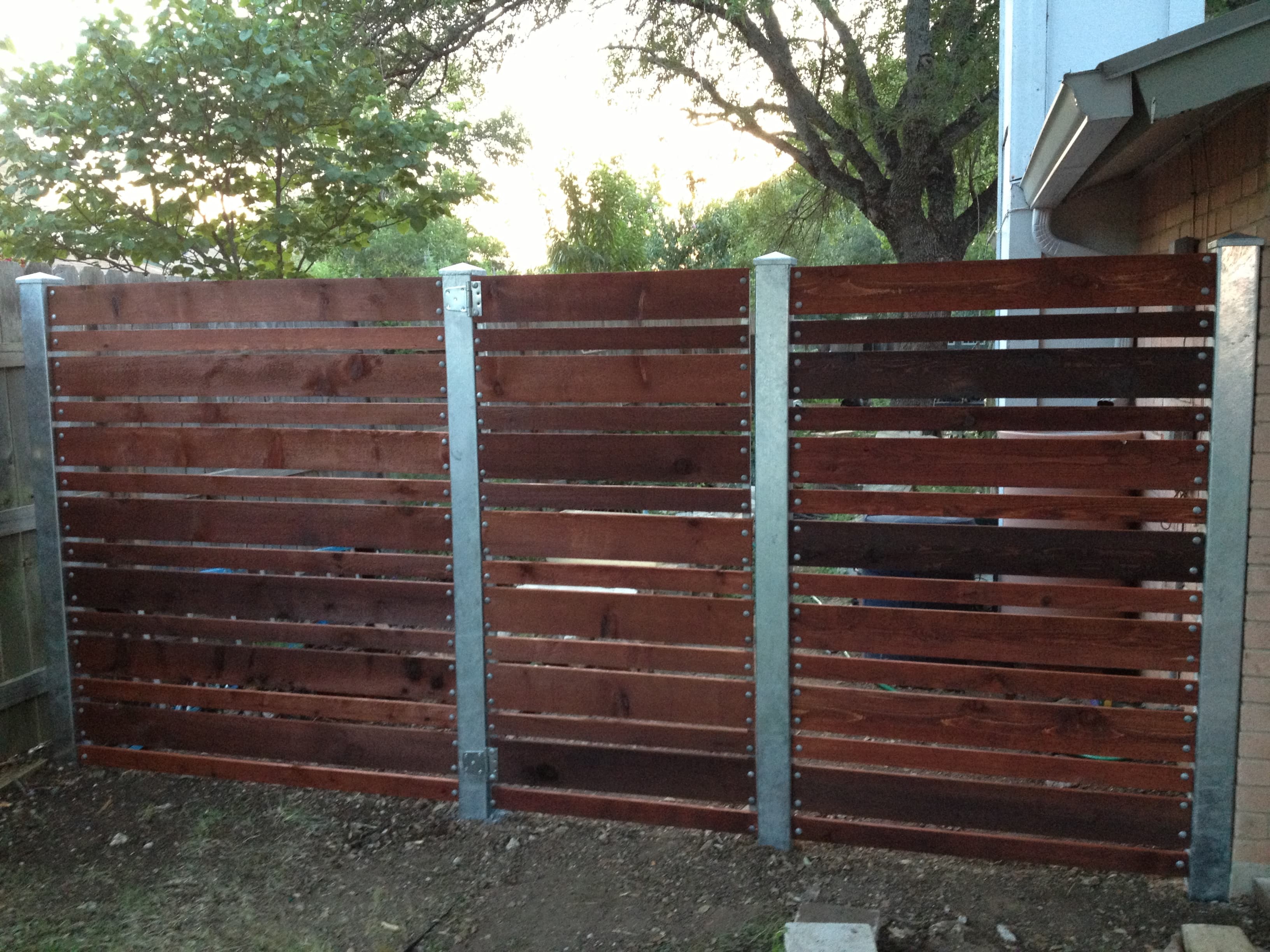 Horizontal cedar privacy fence finished in a rich dark stain and framed by galvanized steel posts for a clean, modern line. The tight horizontal boards and metal posts give this San Antonio backyard a contemporary look while standing up to Texas weather.