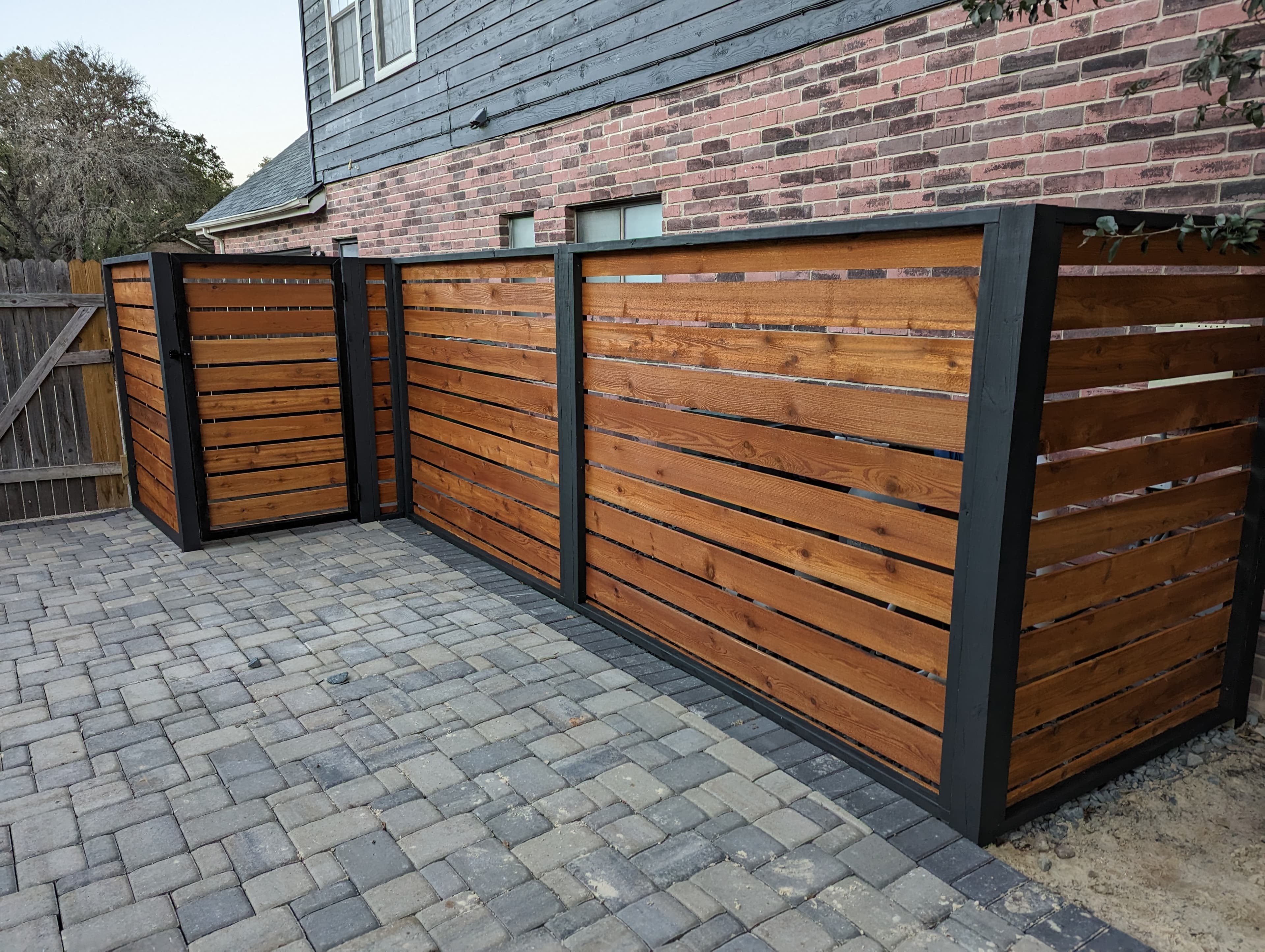 Horizontal cedar slat screen fence in a two-tone stain, dark frame against natural slats